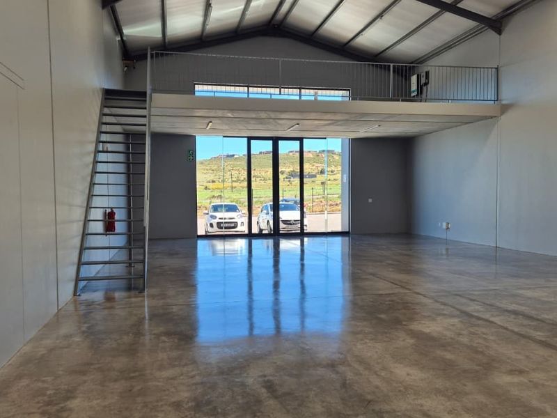 Spacious open-plan retail or industrial unit featuring polished concrete floors, a mezzanine level with metal staircase, and high ceilings with exposed steel trusses.