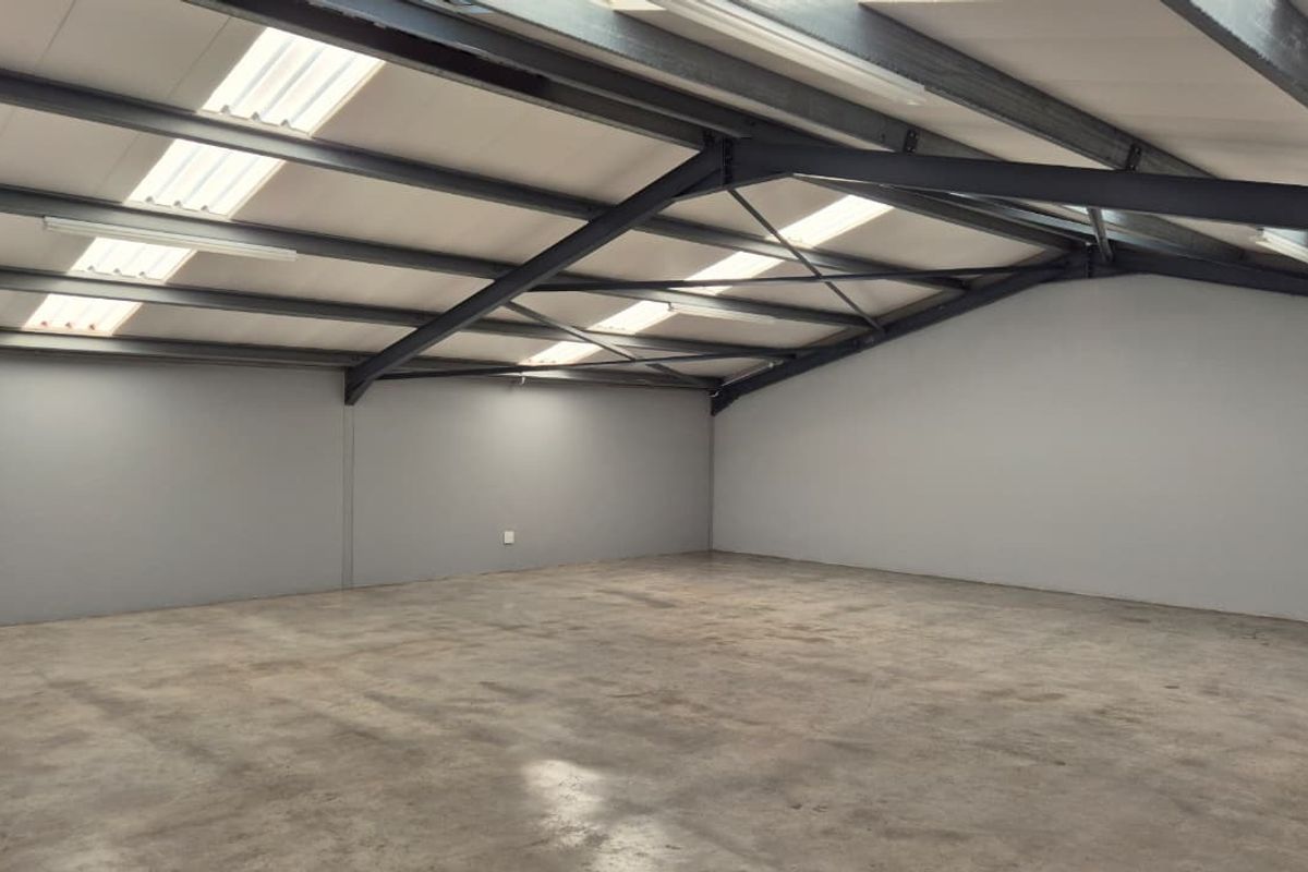 Spacious open-plan retail or industrial unit featuring exposed steel beams, concrete flooring, and natural light from integrated skylights.