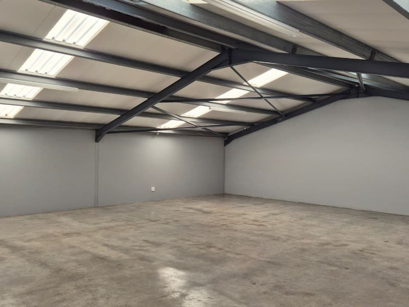 Spacious open-plan retail or industrial unit featuring exposed steel beams, concrete flooring, and natural light from integrated skylights.