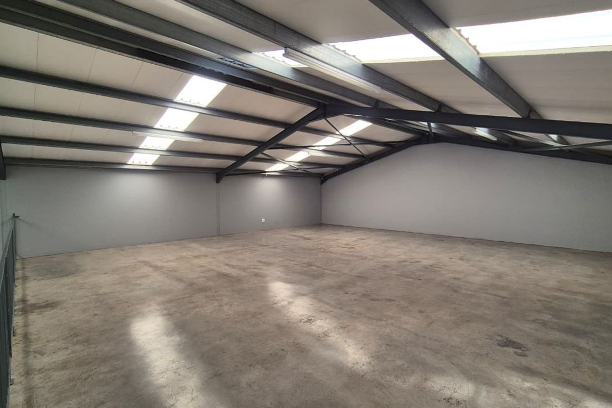 Spacious open-plan utility area featuring exposed steel roof trusses, integrated skylights, and durable concrete flooring, suitable for various commercial or storage applications.