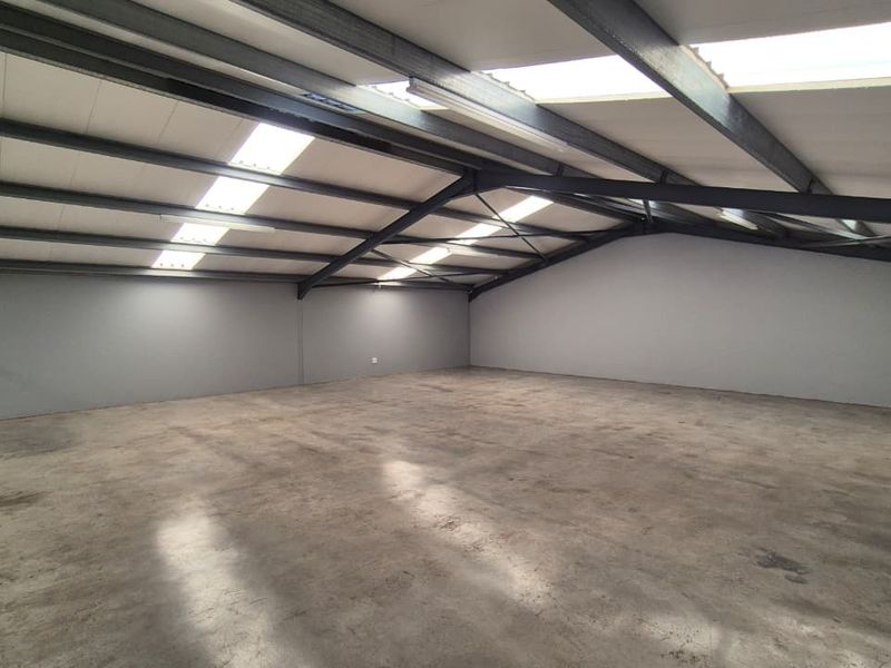 Spacious open-plan utility area featuring exposed steel roof trusses, integrated skylights, and durable concrete flooring, suitable for various commercial or storage applications.
