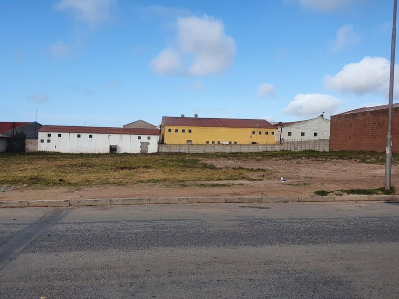 A vacant commercial land plot featuring a level surface, concrete curbing, and direct street access, situated in an established industrial area.