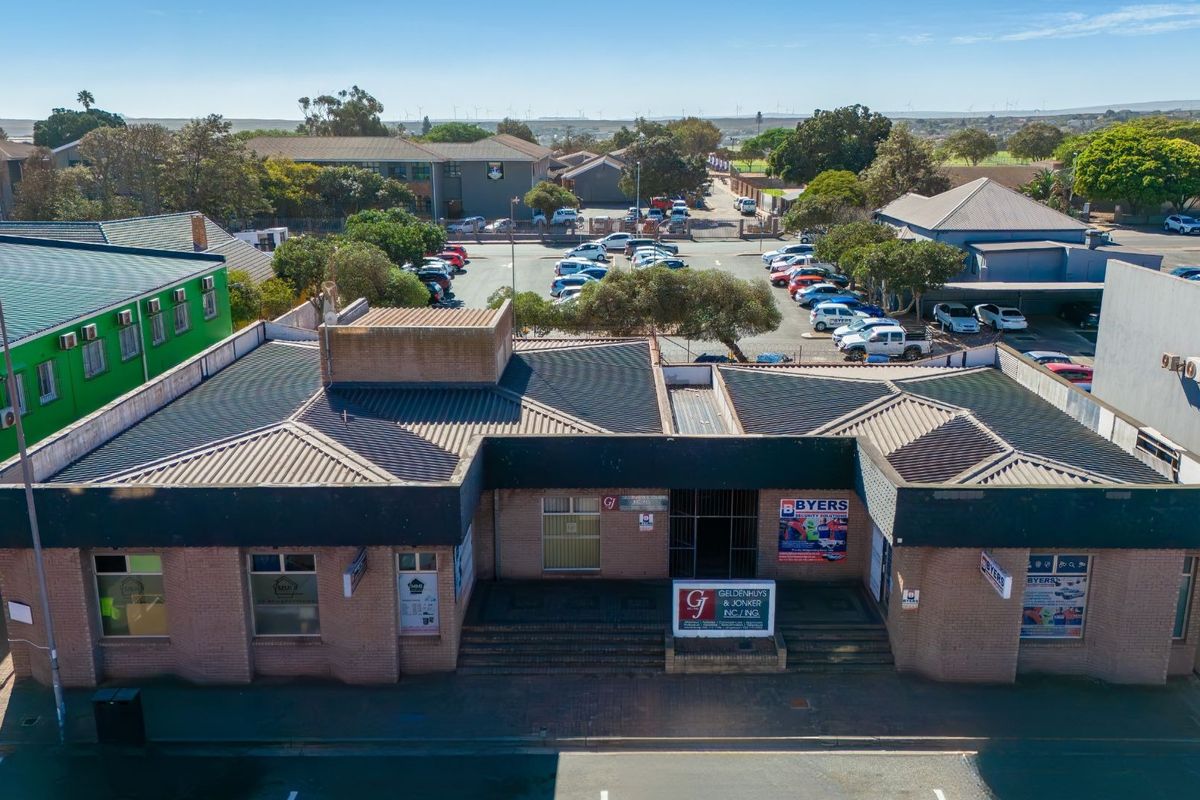 Aerial view of a commercial brick building featuring a corrugated metal roof, paved entrance steps, and prominent street-level signage.