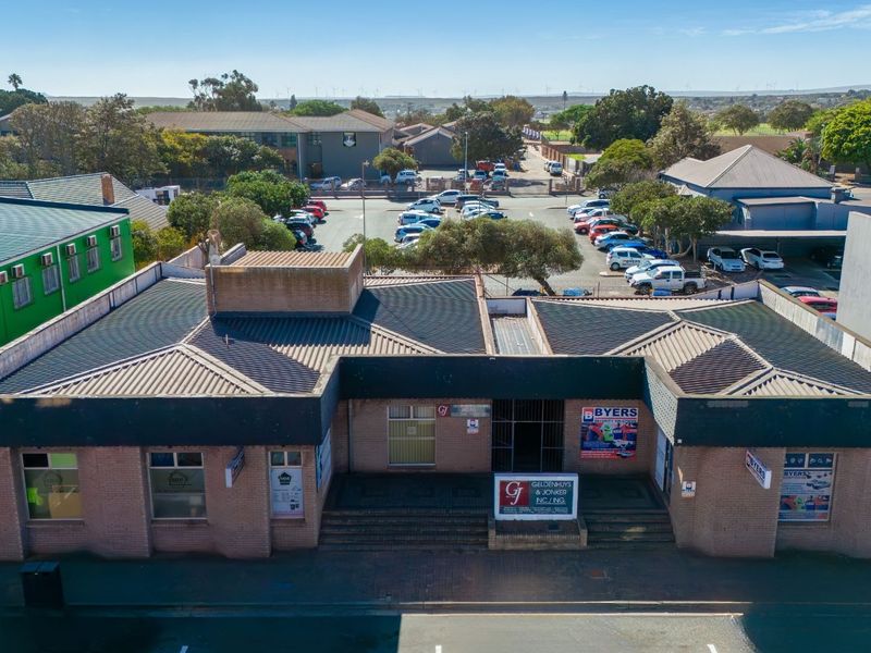 Aerial view of a commercial brick building featuring a corrugated metal roof, paved entrance steps, and prominent street-level signage.