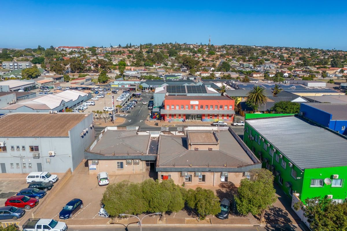 Aerial view of a commercial property complex featuring multiple buildings, metal roofing, external air conditioning units, and an asphalt parking area.