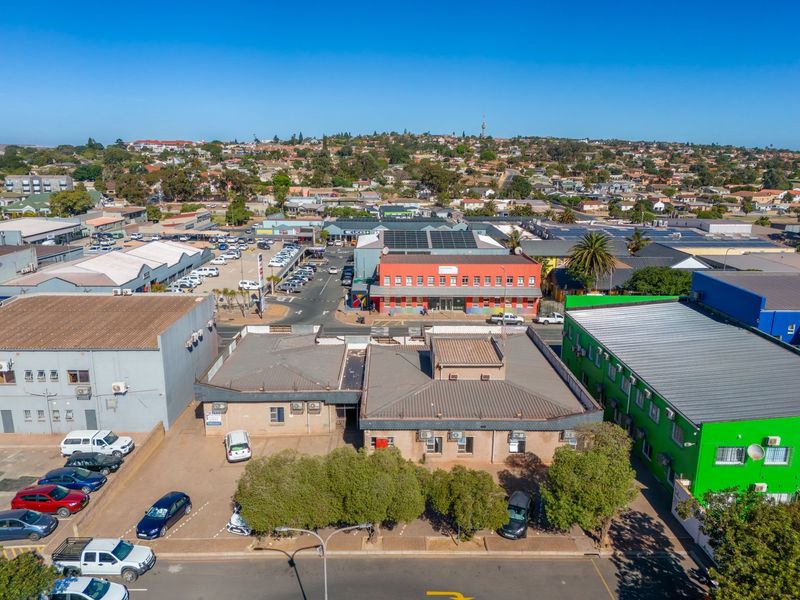 Aerial view of a commercial property complex featuring multiple buildings, metal roofing, external air conditioning units, and an asphalt parking area.