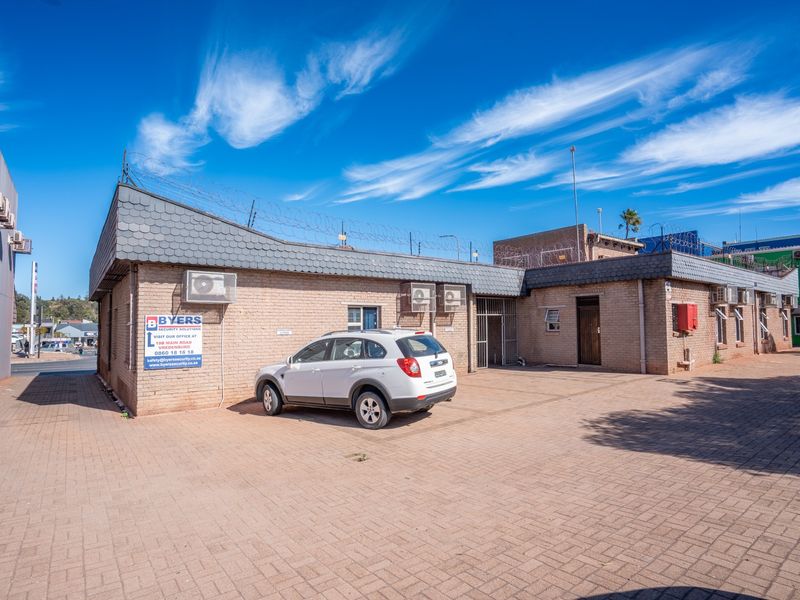 Commercial property exterior featuring a brick facade, paved driveway, security fencing, and multiple wall-mounted air conditioning units.