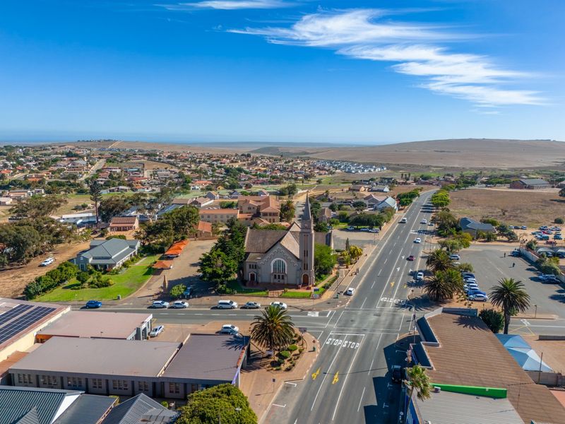 Aerial view of a commercial area featuring a prominent church, surrounding infrastructure, and main road access within a coastal town setting.