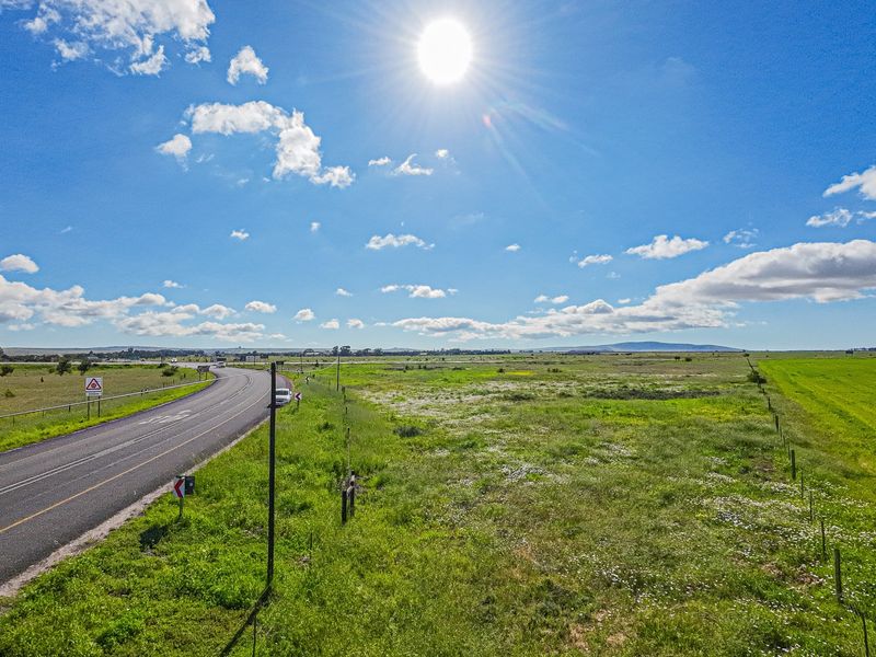 Aerial view of a large vacant commercial land parcel adjacent to a paved road with clear visibility and open landscape.