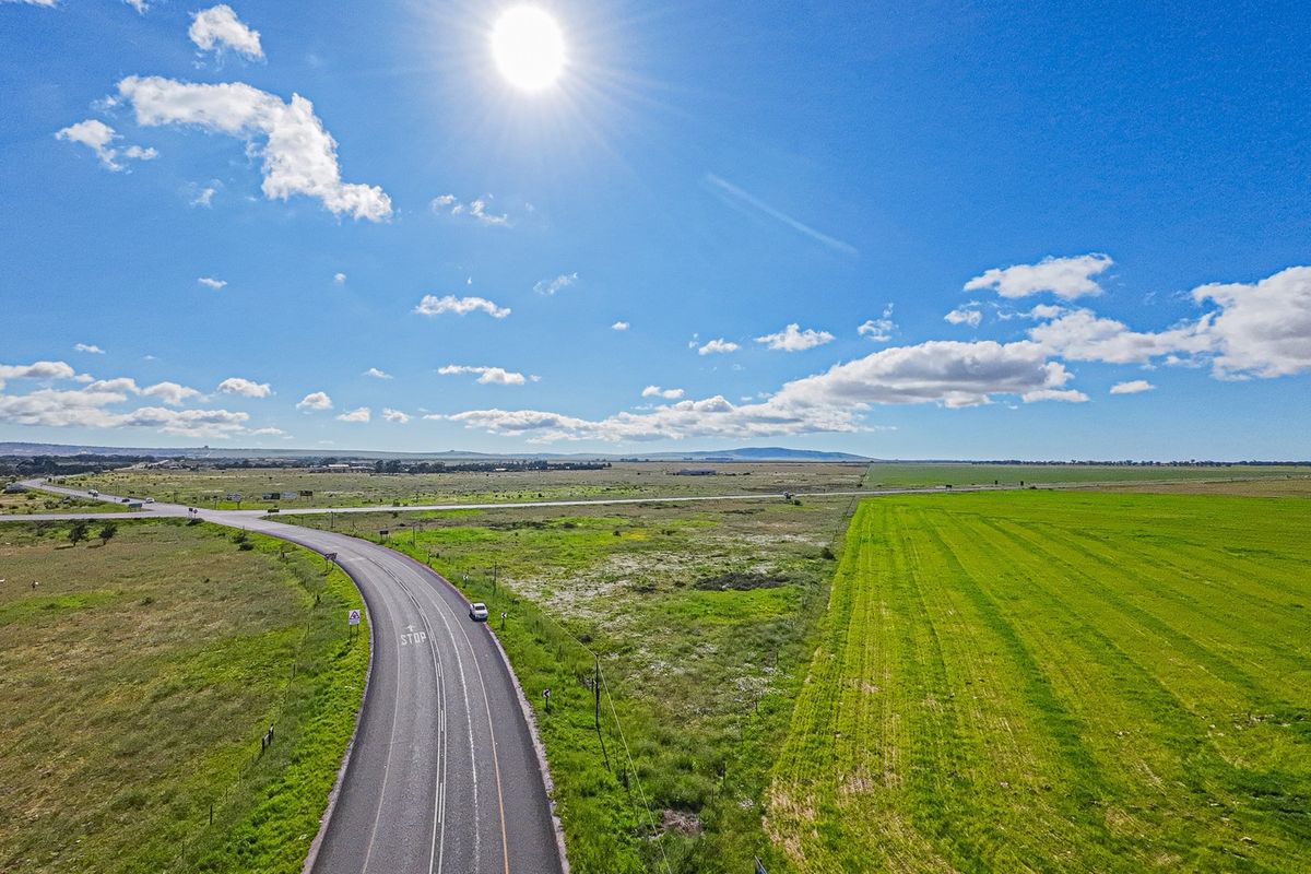 Aerial view of a large commercial vacant land parcel featuring expansive open grassland and direct access to an adjacent asphalt road.