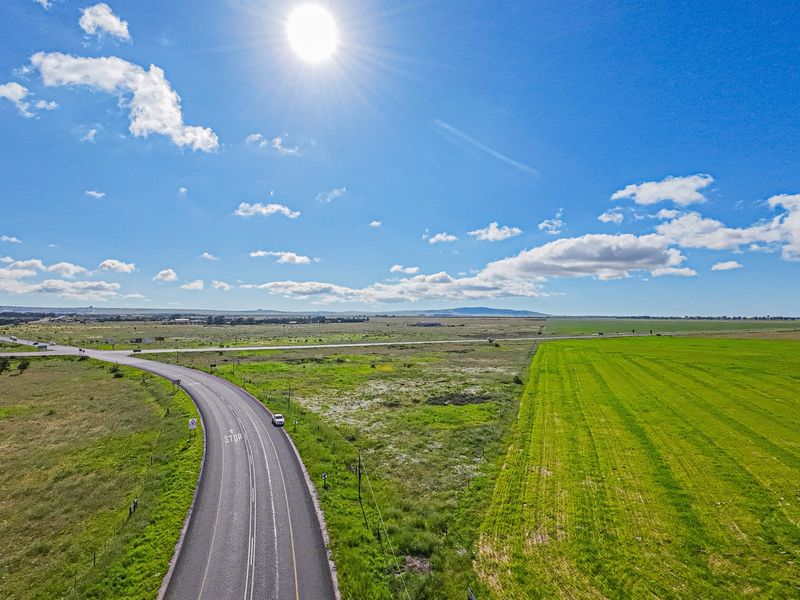 Aerial view of a large commercial vacant land parcel featuring expansive open grassland and direct access to an adjacent asphalt road.