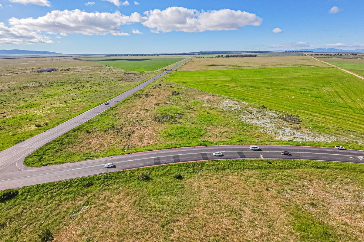 An aerial view of a large, undeveloped commercial land parcel situated at a road intersection, featuring expansive open fields and surrounding rural landscape.