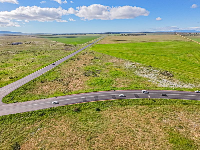 An aerial view of a large, undeveloped commercial land parcel situated at a road intersection, featuring expansive open fields and surrounding rural landscape.