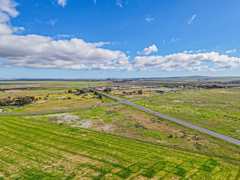 An aerial view of a large, undeveloped commercial land parcel situated at a prominent road intersection, offering significant potential for future development.