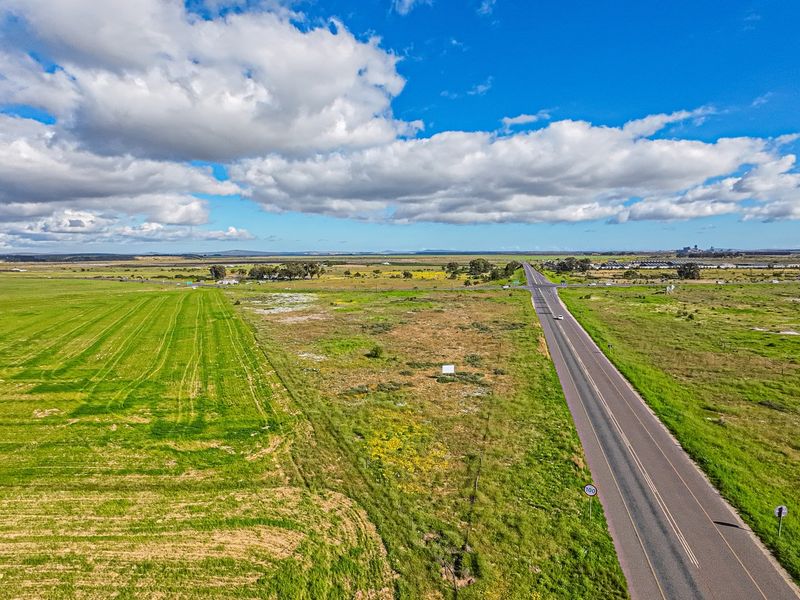Aerial view of expansive vacant commercial land adjacent to a main road, offering significant development potential and high visibility.
