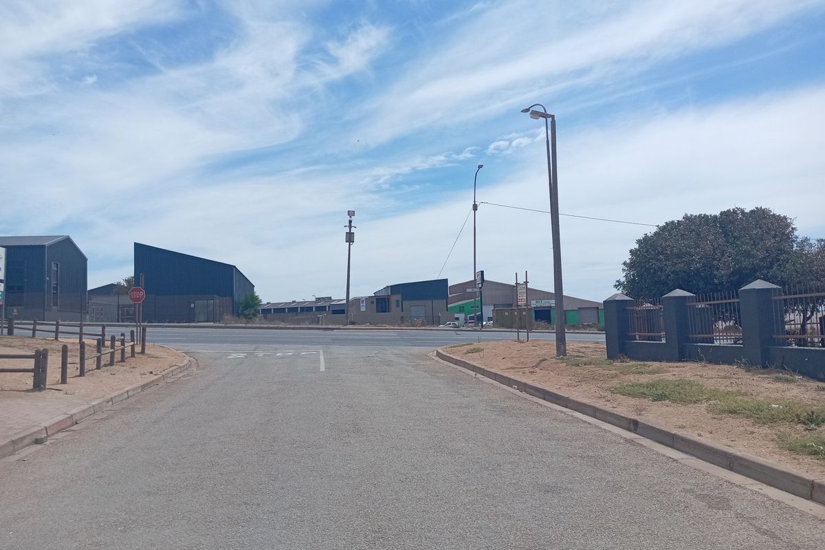 A street-level view of the commercial property access road, featuring paved surfaces, perimeter fencing, and surrounding industrial infrastructure.