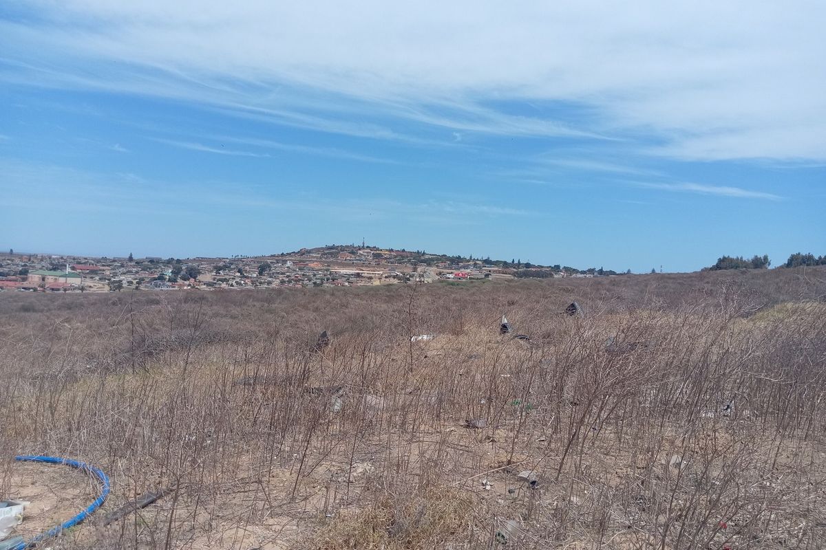 An elevated view overlooking a vacant commercial land plot with dry vegetation and distant residential development.