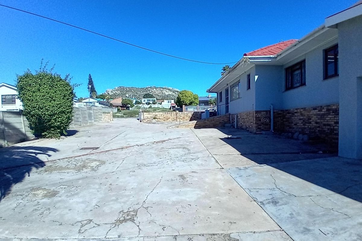 Rear exterior view of the commercial property featuring a large concrete driveway, brick facade, and metal roofing with surrounding boundary walls.