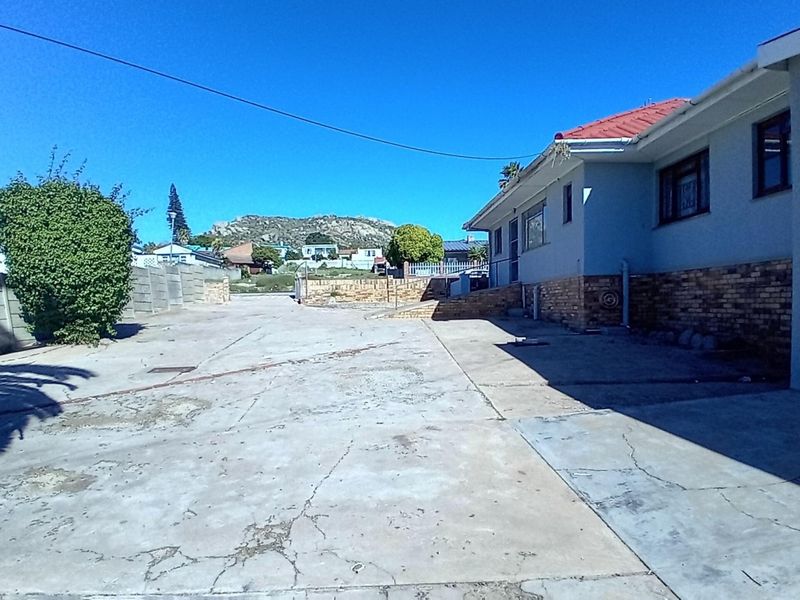 Rear exterior view of the commercial property featuring a large concrete driveway, brick facade, and metal roofing with surrounding boundary walls.