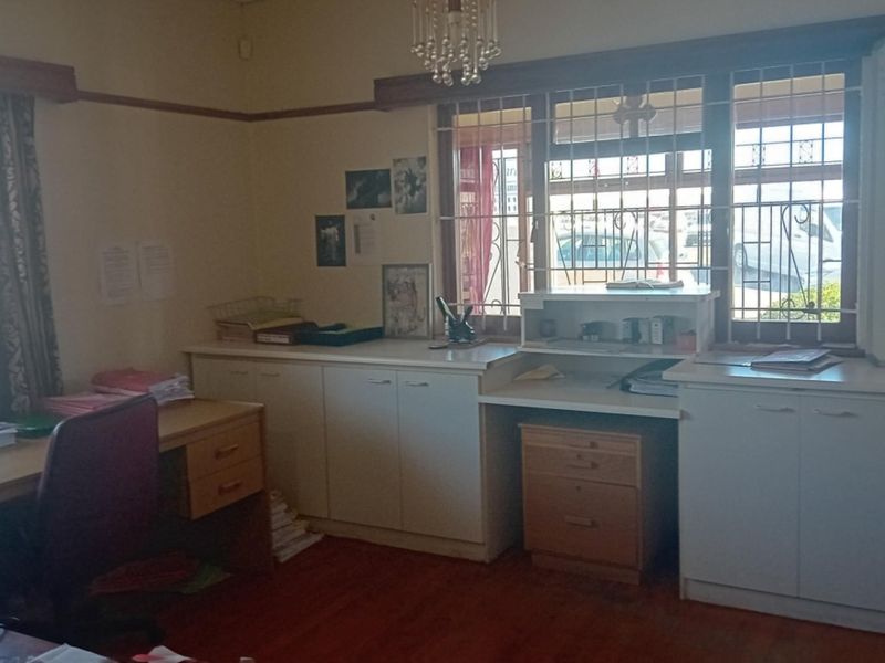 A functional office space featuring built-in cabinetry, timber flooring, and windows fitted with security bars.