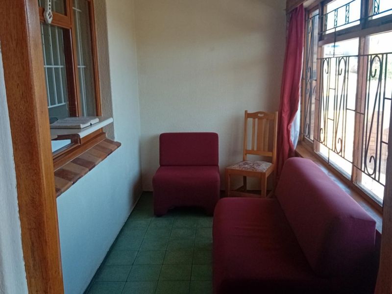 A sunroom or enclosed patio area featuring tiled flooring, wooden window frames with security bars, and natural light.