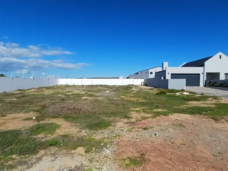 A vacant residential plot featuring a perimeter wall with electric fencing, adjacent to an existing modern home with a paved driveway.