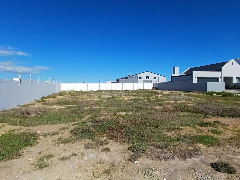 A vacant residential plot featuring a perimeter wall with electric fencing, situated in a developed neighborhood.