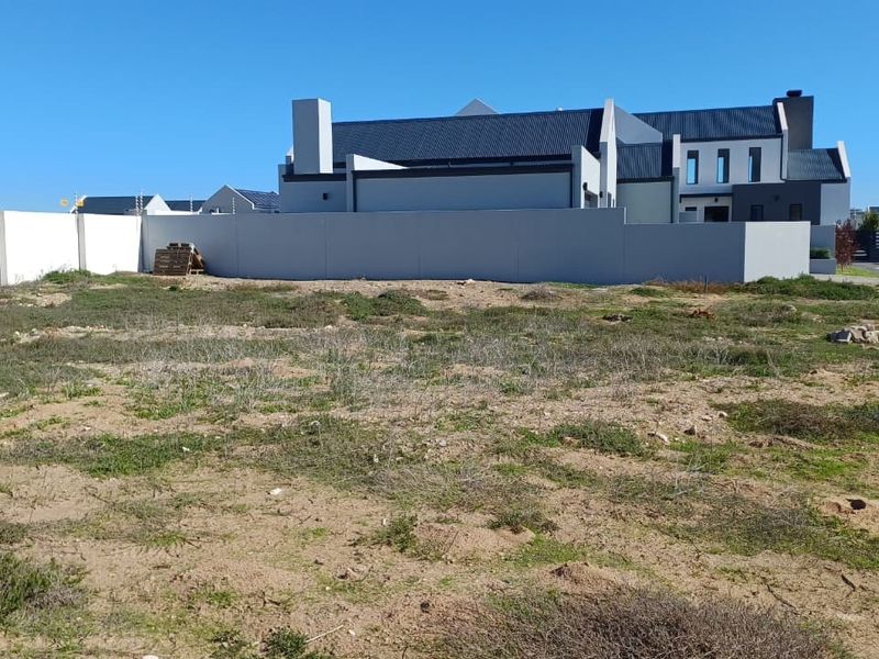A vacant residential plot featuring a perimeter wall with electric fencing, situated in a developed estate setting.