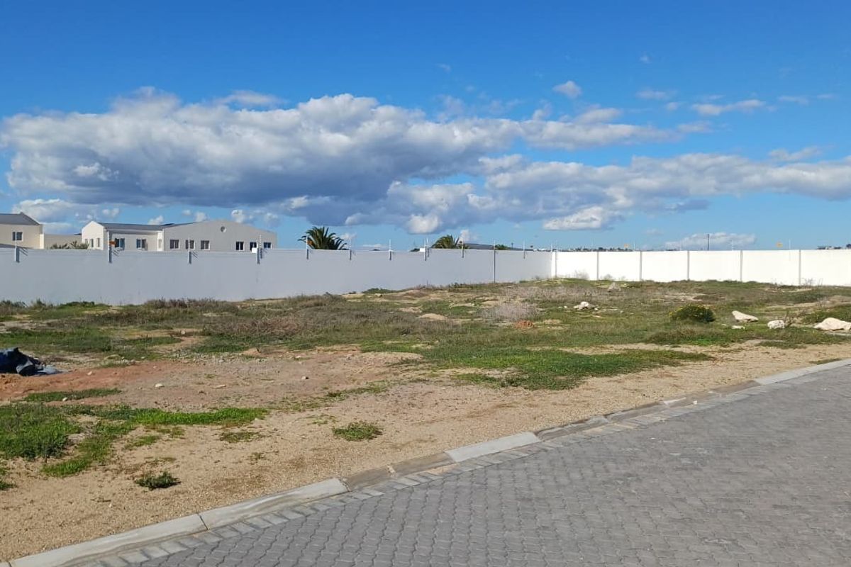 A vacant residential plot featuring a perimeter wall and adjacent paved street access, ready for development.