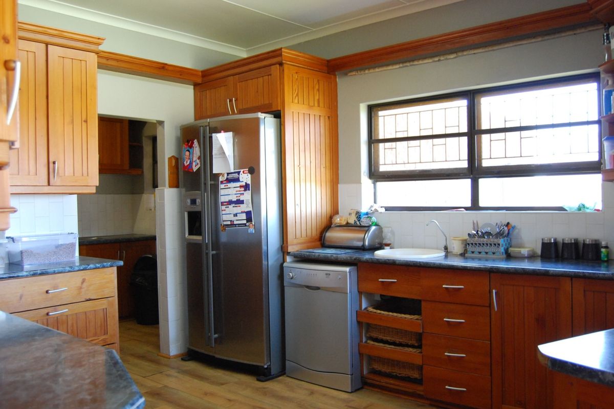 A functional kitchen featuring wooden cabinetry, laminate countertops, and a tiled backsplash, with an adjacent scullery area visible in the background.