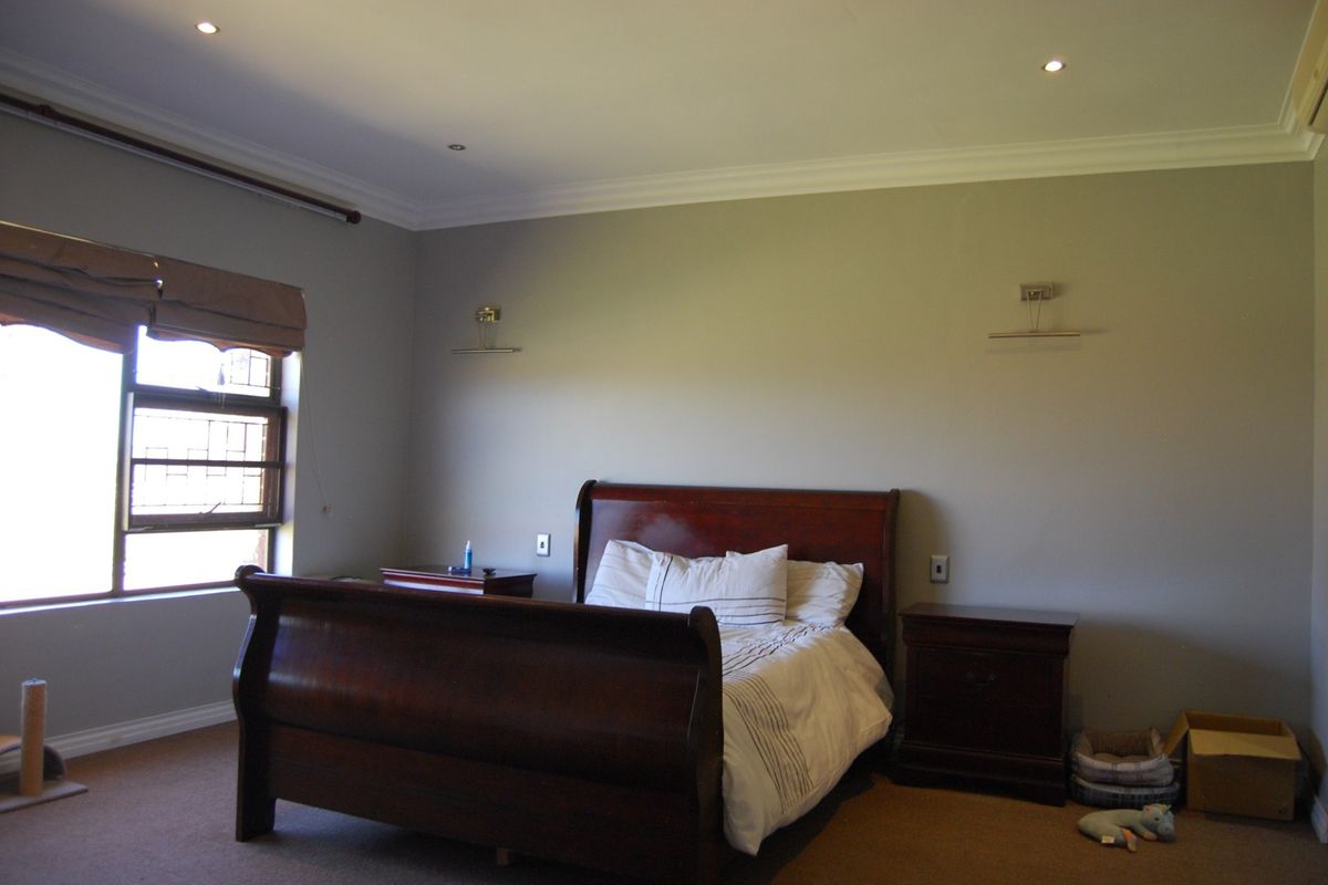 A spacious bedroom featuring neutral wall tones, recessed downlighting, carpeted flooring, and a window fitted with security bars.
