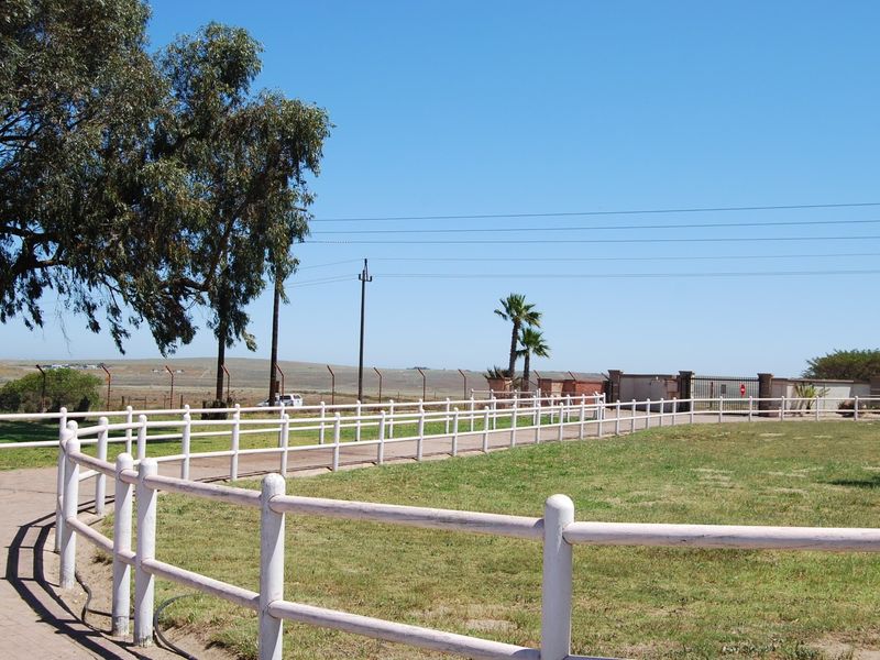 A view of the property entrance featuring a paved driveway, white post and rail fencing, and a secure gated access point on a small holding.