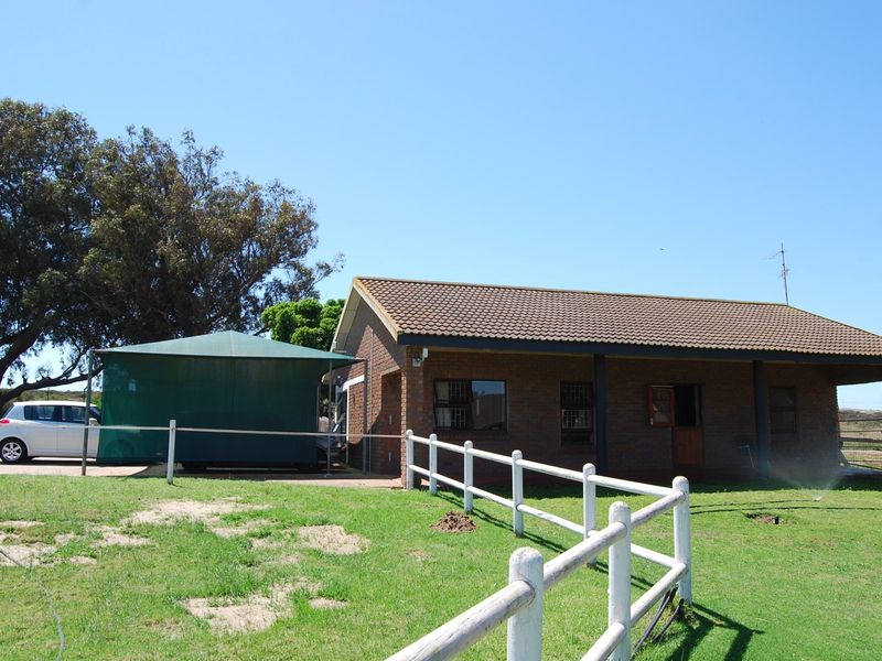 A view of the face-brick exterior of the small holding property, featuring a covered patio, tiled roof, and surrounding lawn with post-and-rail fencing.
