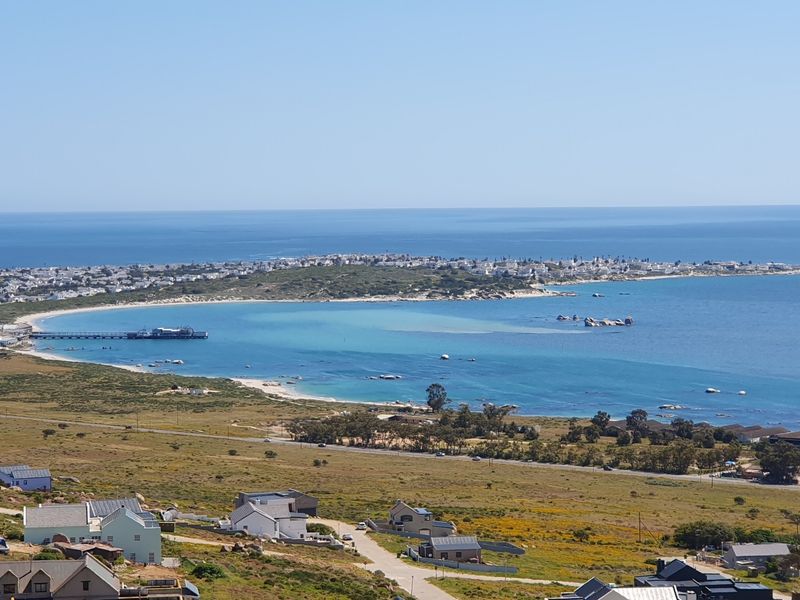 A panoramic elevated view overlooking the coastal landscape, featuring the ocean, sandy beach, and surrounding residential development.