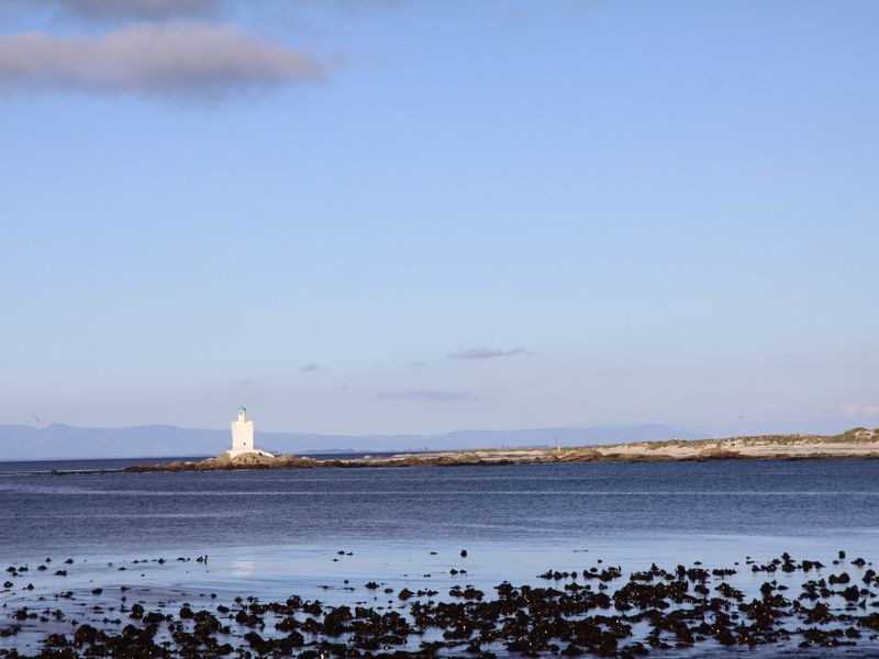 A scenic coastal view featuring the ocean, rocky shoreline, and a distant lighthouse on the horizon.