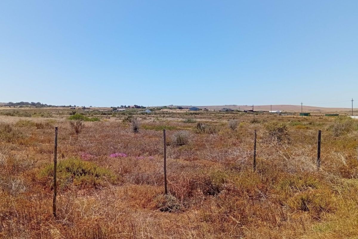 A wide-angle view of the vacant residential land, featuring natural vegetation and perimeter wire fencing under a clear blue sky.