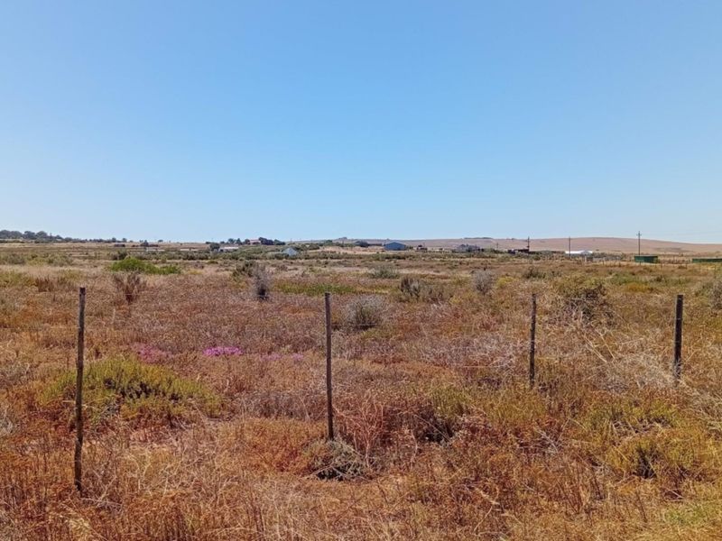A wide-angle view of the vacant residential land, featuring natural vegetation and perimeter wire fencing under a clear blue sky.