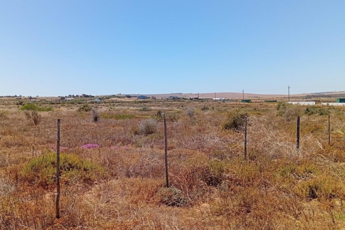 A wide-angle view of a vacant residential plot featuring natural vegetation and simple wire perimeter fencing.