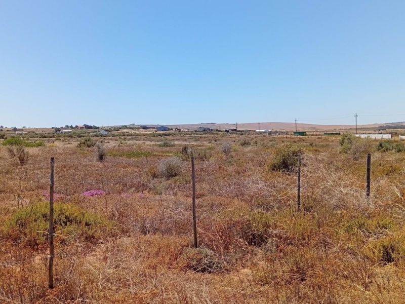 A wide-angle view of a vacant residential plot featuring natural vegetation and simple wire perimeter fencing.