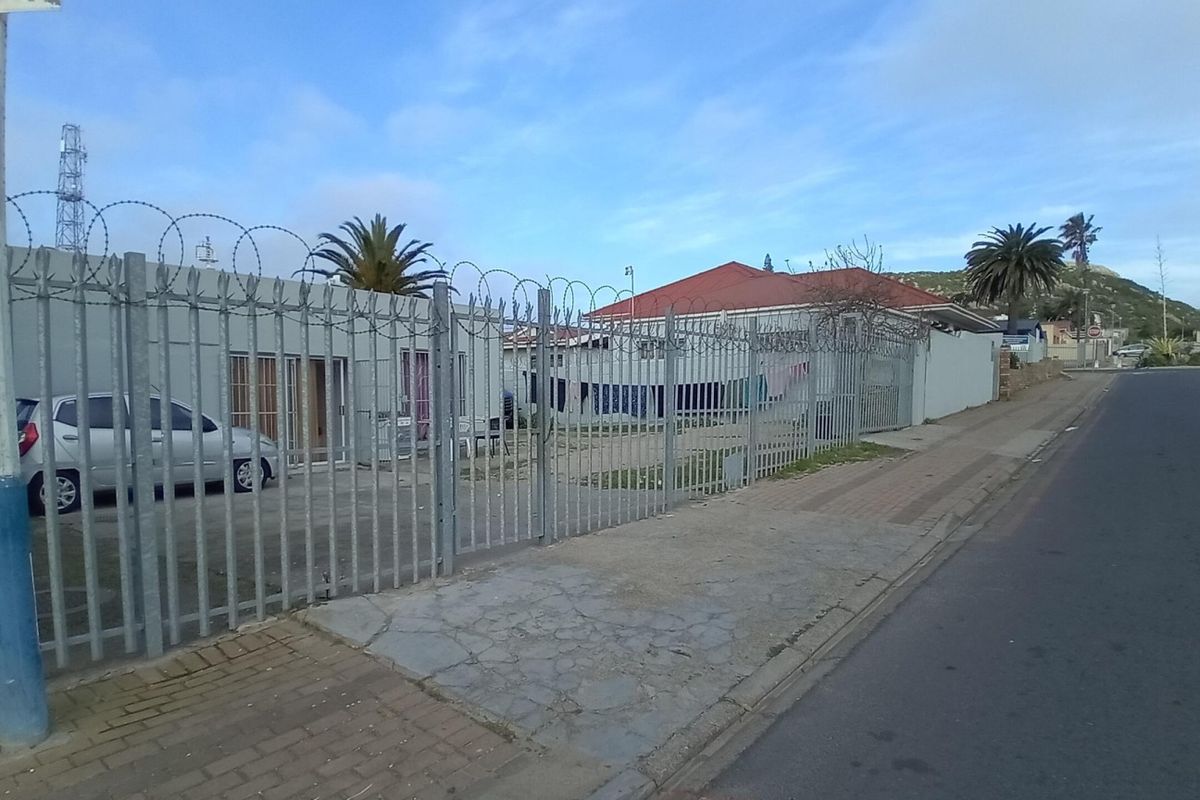 Street view of a commercial property featuring secure metal perimeter fencing with razor wire and a paved sidewalk.