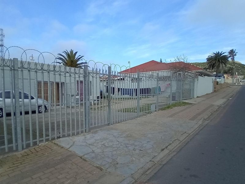 Street view of a commercial property featuring secure metal perimeter fencing with razor wire and a paved sidewalk.