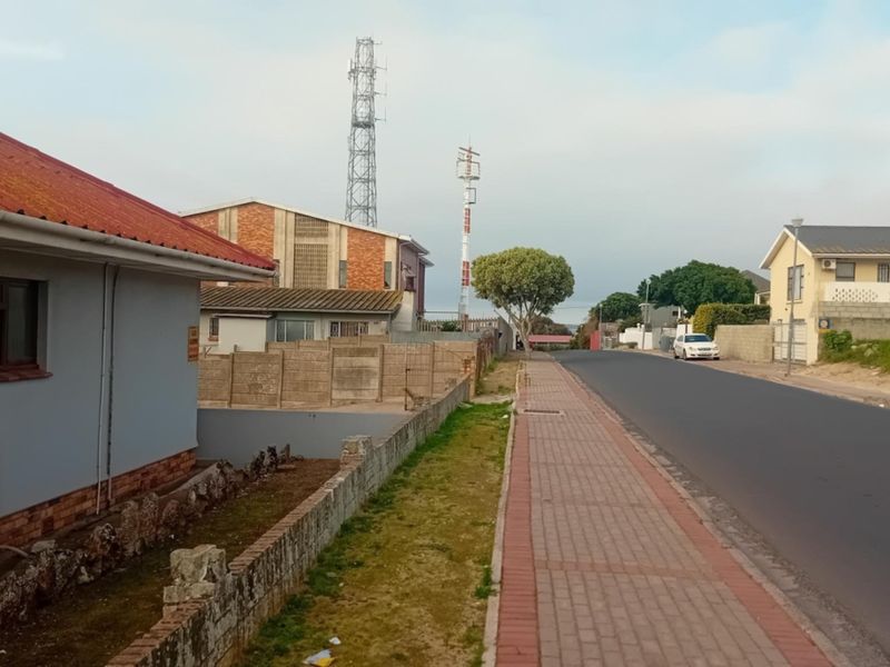 A street-level view showing the paved sidewalk, asphalt road, and surrounding commercial and residential properties with visible telecommunication infrastructure.