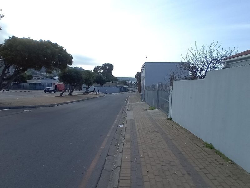 A street-level view showing the paved sidewalk, perimeter wall with security fencing, and adjacent asphalt road in a commercial area.