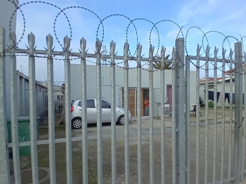 Front view of a commercial property featuring a secure galvanized steel palisade fence with razor wire and a concrete driveway entrance.
