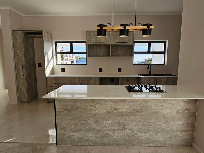 Modern kitchen featuring textured cabinetry, stone countertops, a built-in gas hob, and sleek pendant lighting in an open-plan layout.