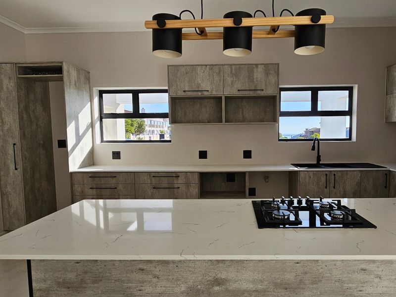 Modern kitchen featuring wood-look cabinetry, stone countertops, a central island with a gas hob, and contemporary black fixtures.