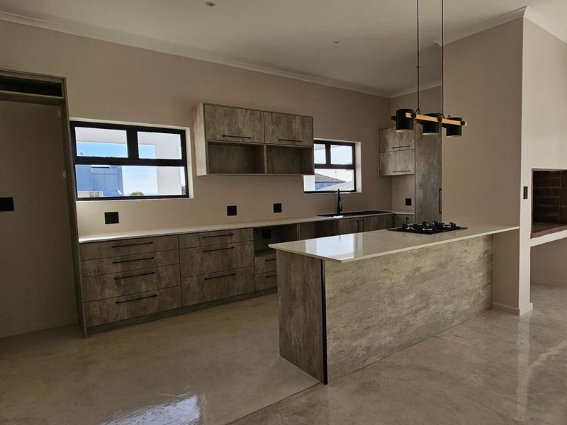 Modern open-plan kitchen featuring textured cabinetry, stone countertops, gas hob, and a built-in indoor braai area, finished with polished concrete flooring.