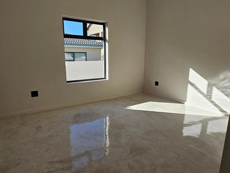 A bright, empty bedroom featuring polished concrete flooring and a modern aluminium window, offering a clean and neutral space ready for personalization.