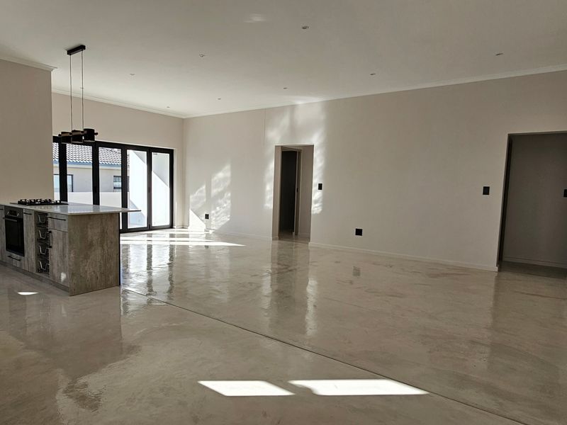 Spacious open-plan living area featuring polished concrete floors, recessed lighting, and a modern kitchen island with built-in oven and gas cooktop.