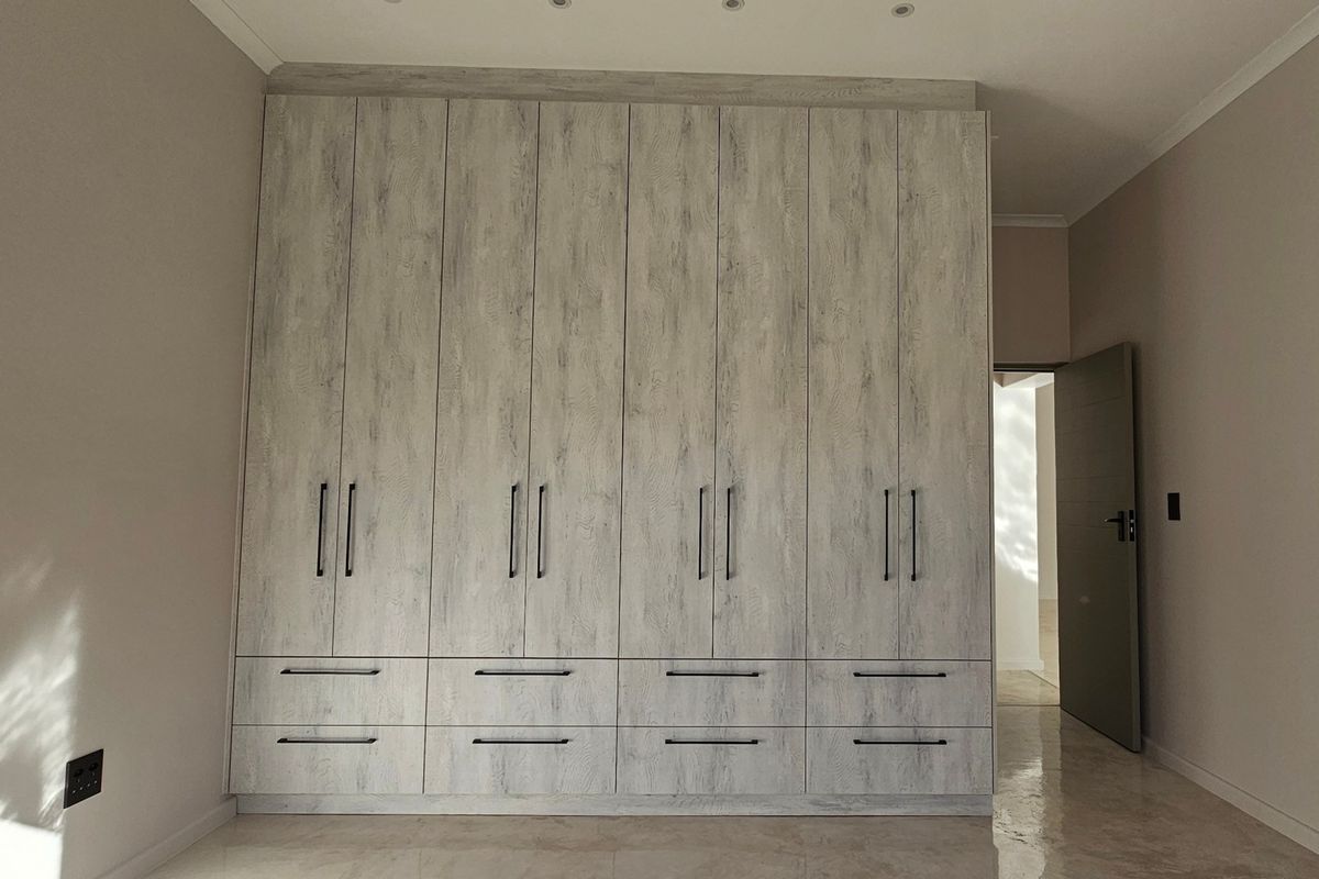 A spacious bedroom featuring extensive floor-to-ceiling built-in cupboards with a modern wood-grain finish, recessed lighting, and polished tiled flooring.
